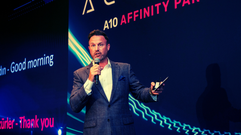 The keynote speaker at A10 Networks partner event. A man with a microphone on stage in front of A10 branded signage