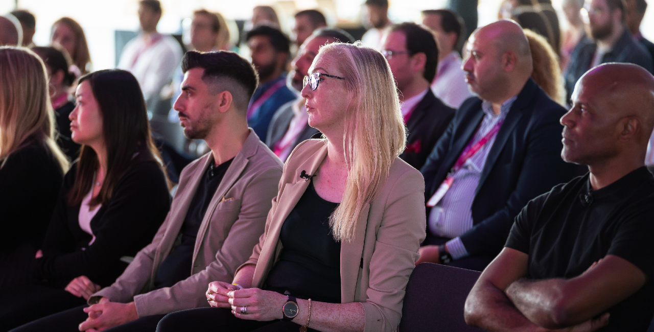 A diverse group of professionals seated in an audience at an event, listening to a presentation.
